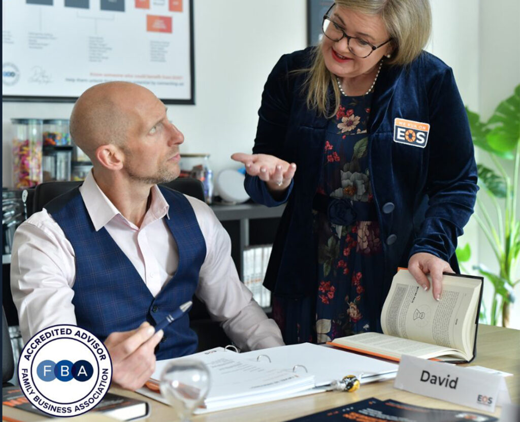 Woman showing a book to a man seated at a desk during a business discussion.